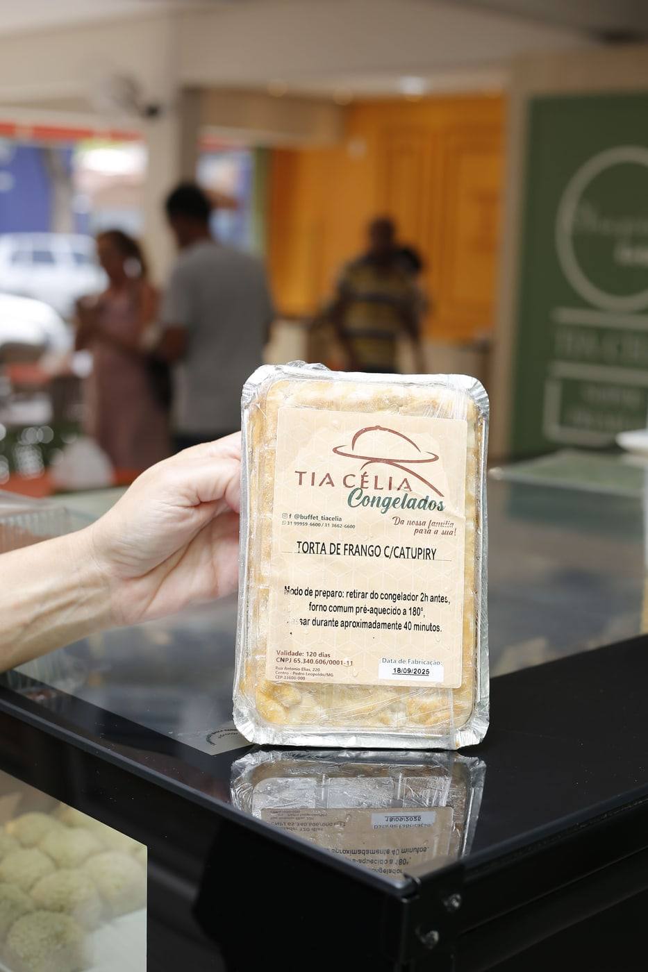 Mão segurando a embalagem de torta de frango com catupiry da linha Tia Célia Congelados.