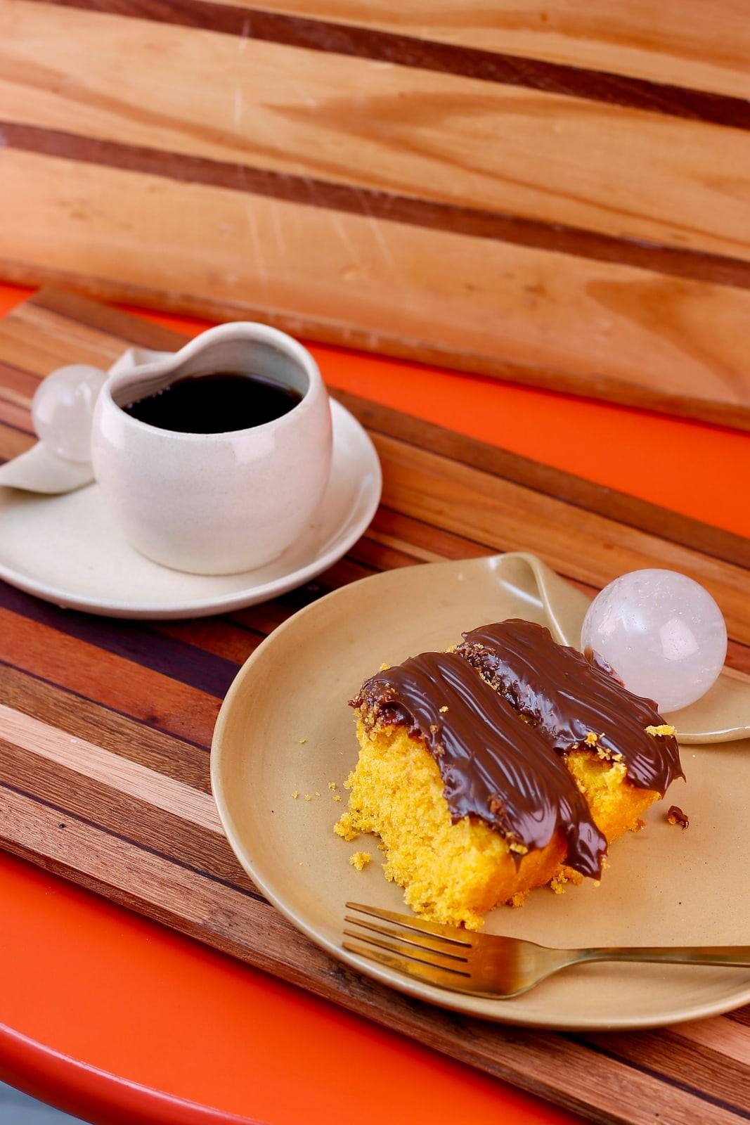 Fatia de bolo de cenoura com cobertura de brigadeiro ao lado de uma xícara de café.