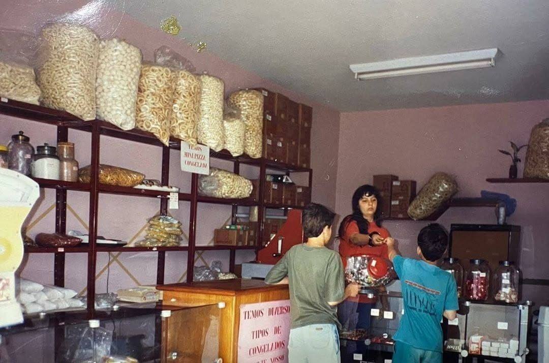Interior antigo da GelaGuela, com prateleiras de produtos e clientes no balcão.