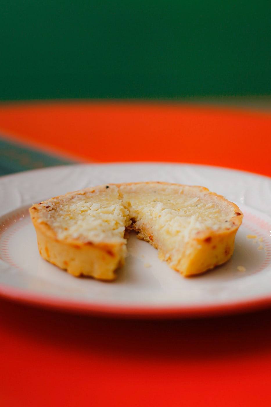 Quiche de quatro queijos cortada, servida em prato branco sobre a mesa laranja.