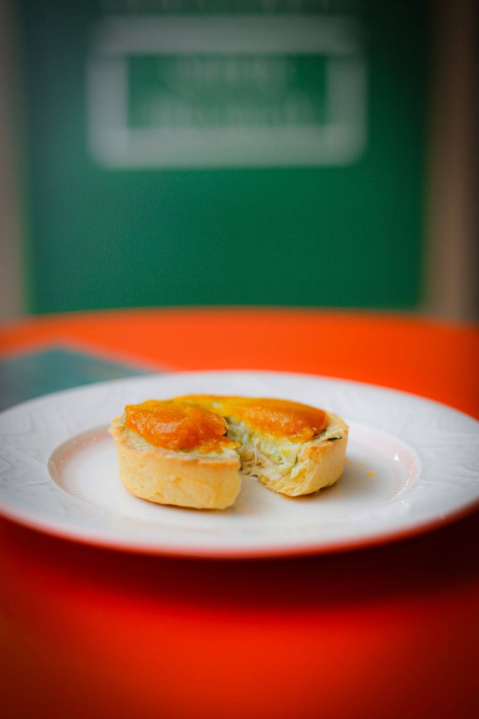 Quiche de alho-poró com damasco servida em prato branco sobre a mesa laranja.