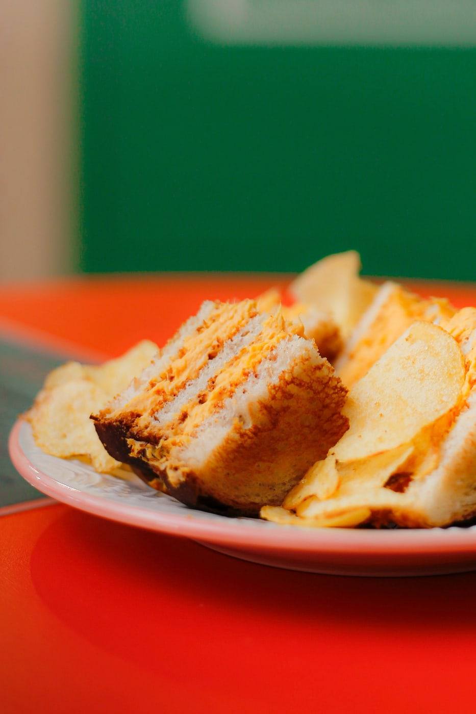 Sanduíche de galinha cortado ao meio servido com batata chips sobre a mesa laranja da loja.