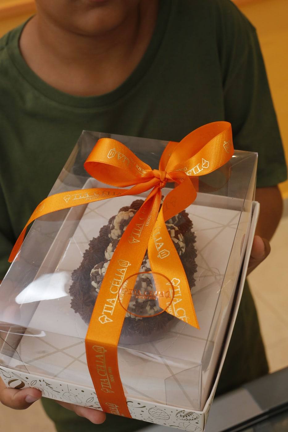 Ovo de Páscoa da Tia Célia embalado em caixa transparente com laço de fita laranja.